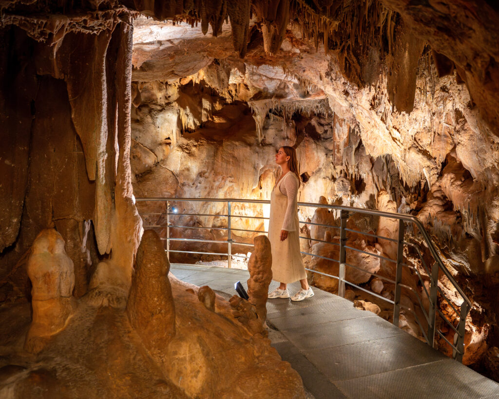 A woman walking inside Petralona Cave admiring the stalagmites & stalactites